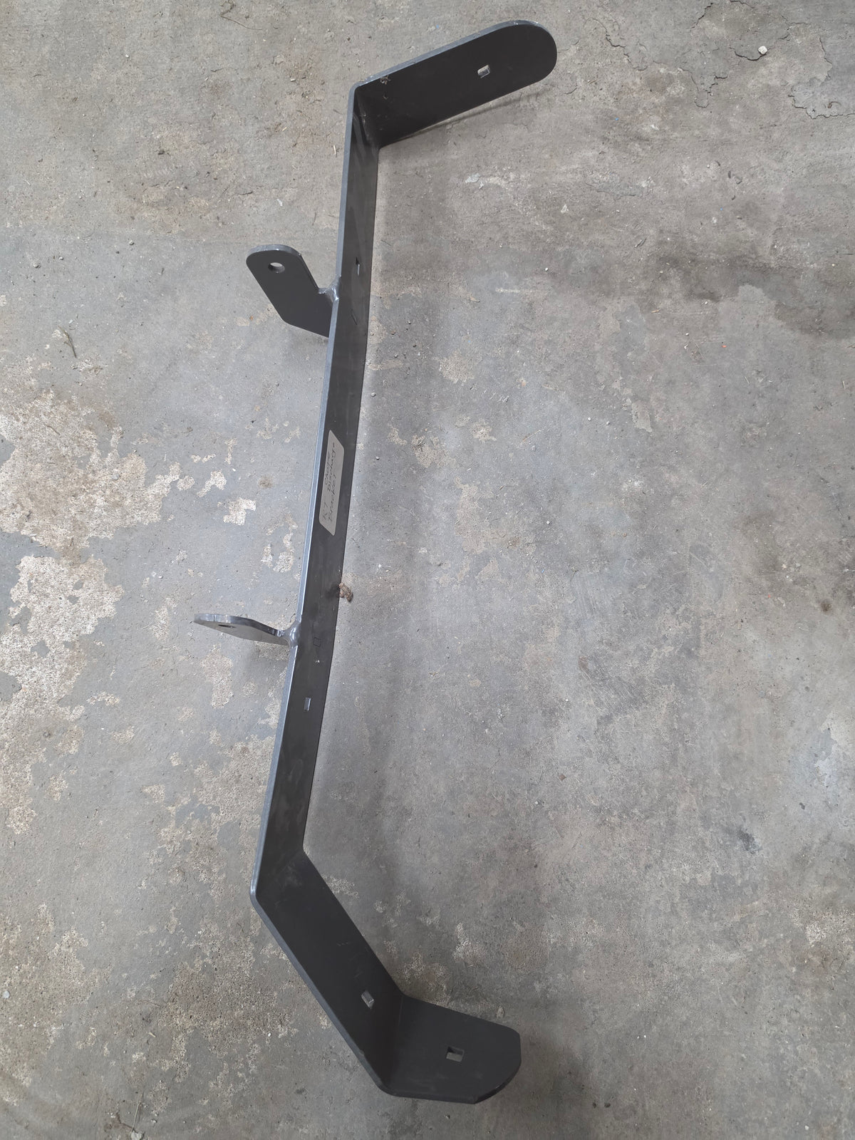 A black metal mounting bracket or frame component photographed on a concrete floor.