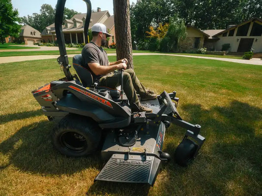 Person operating a lawn mower on a grassy area with trees and houses in the background
