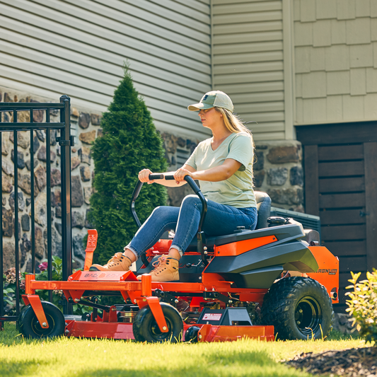 Person operating a red riding lawn mower in a residential backyard.