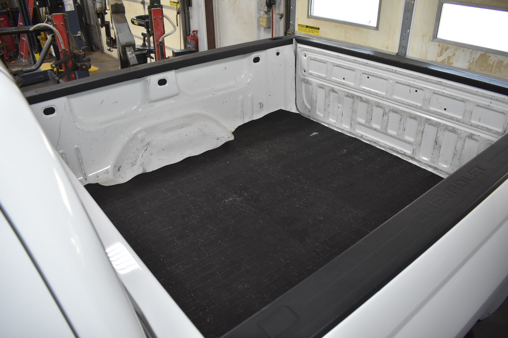 Black bed liner in a white truck bed with tools and equipment in the background