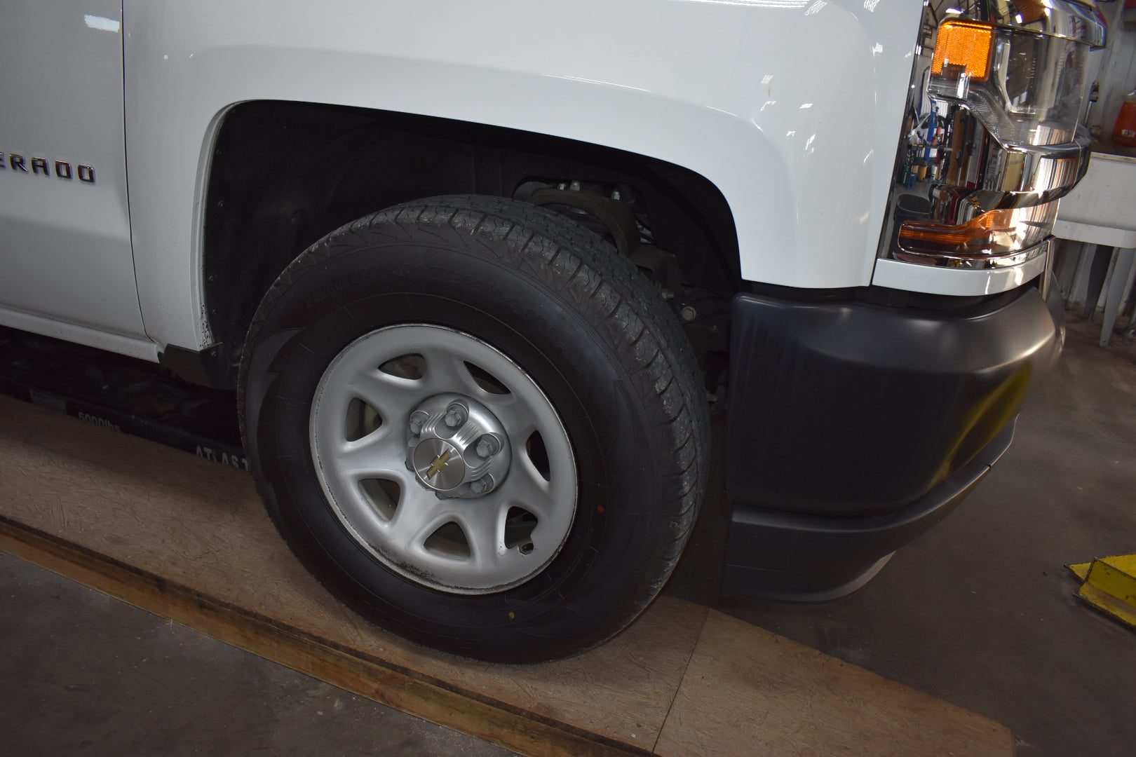 Close-up of a white truck's front wheel and bumper in a garage setting