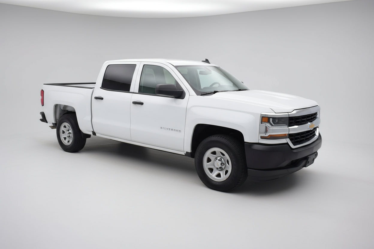 White Chevrolet Silverado truck parked in a parking lot with a gas station in the background.