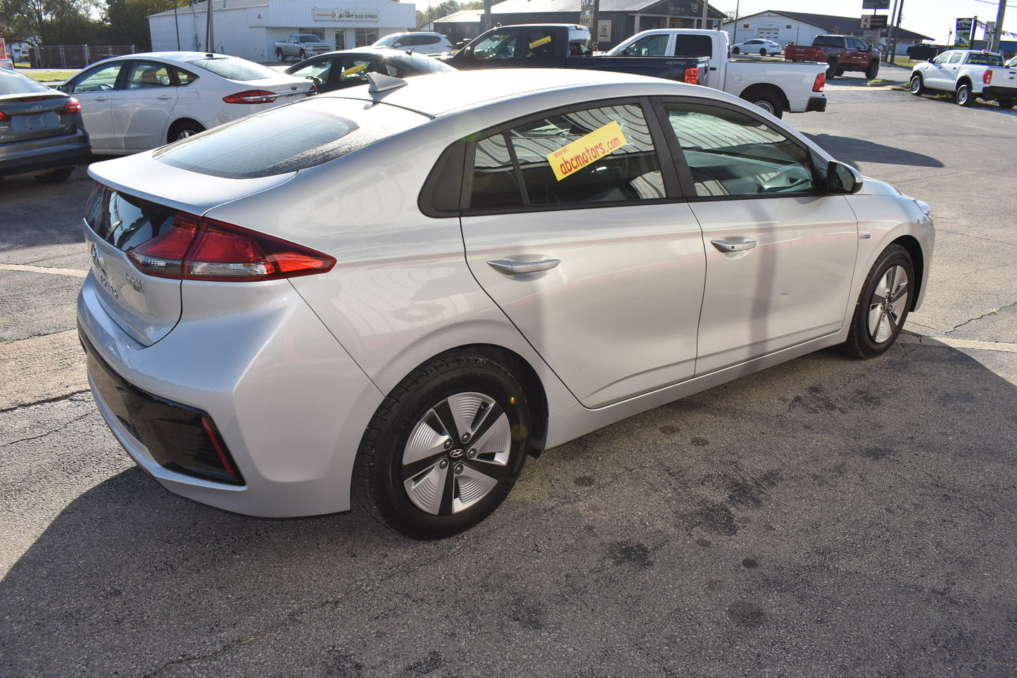 White car parked on a concrete surface with other vehicles in the background