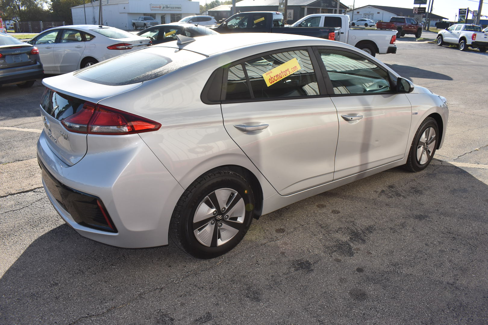 White car parked on a concrete surface with other vehicles in the background