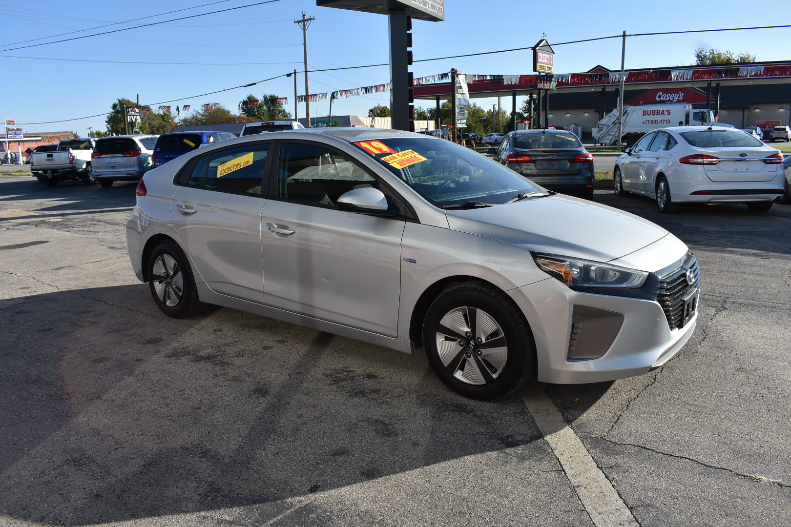 White car parked in a gas station lot with other vehicles and a clear sky.