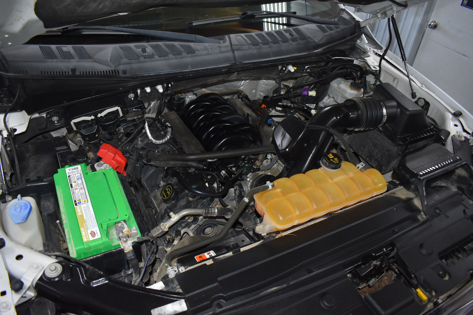 Open car hood revealing engine compartment with various components.
