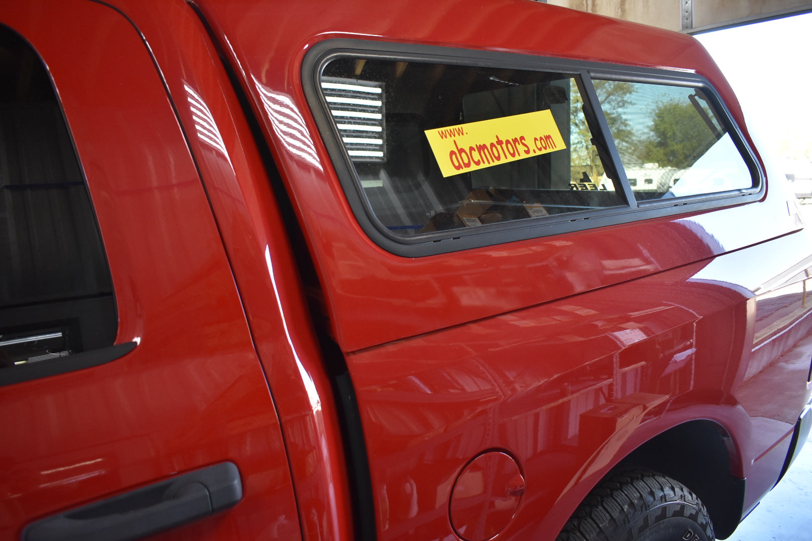 Red vehicle with a window sticker displaying 'abcmotors.com' in a showroom setting