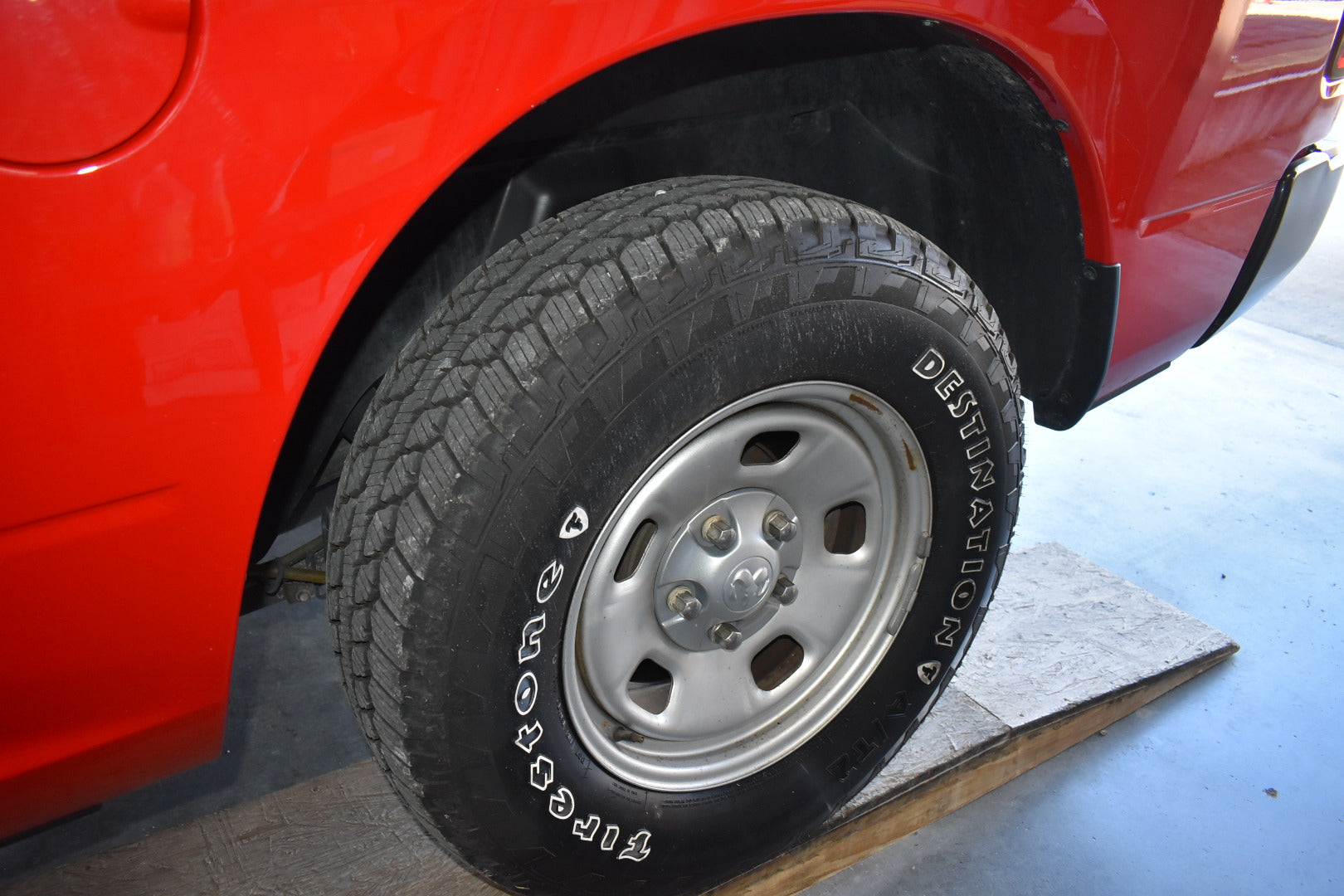 Close-up of a red vehicle's tire with a spare tire on a stand.