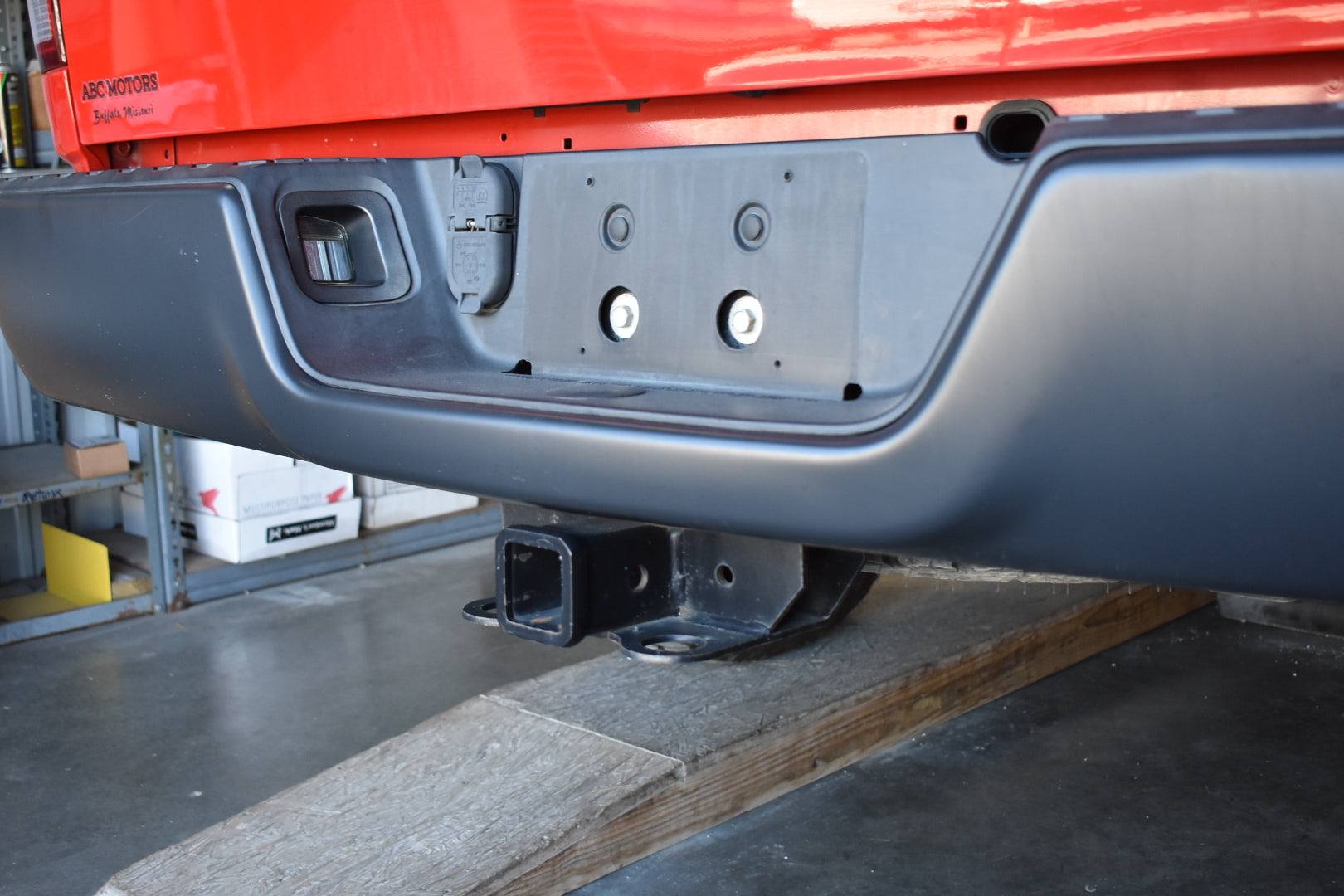 Close-up of a vehicle bumper with a red truck in the background