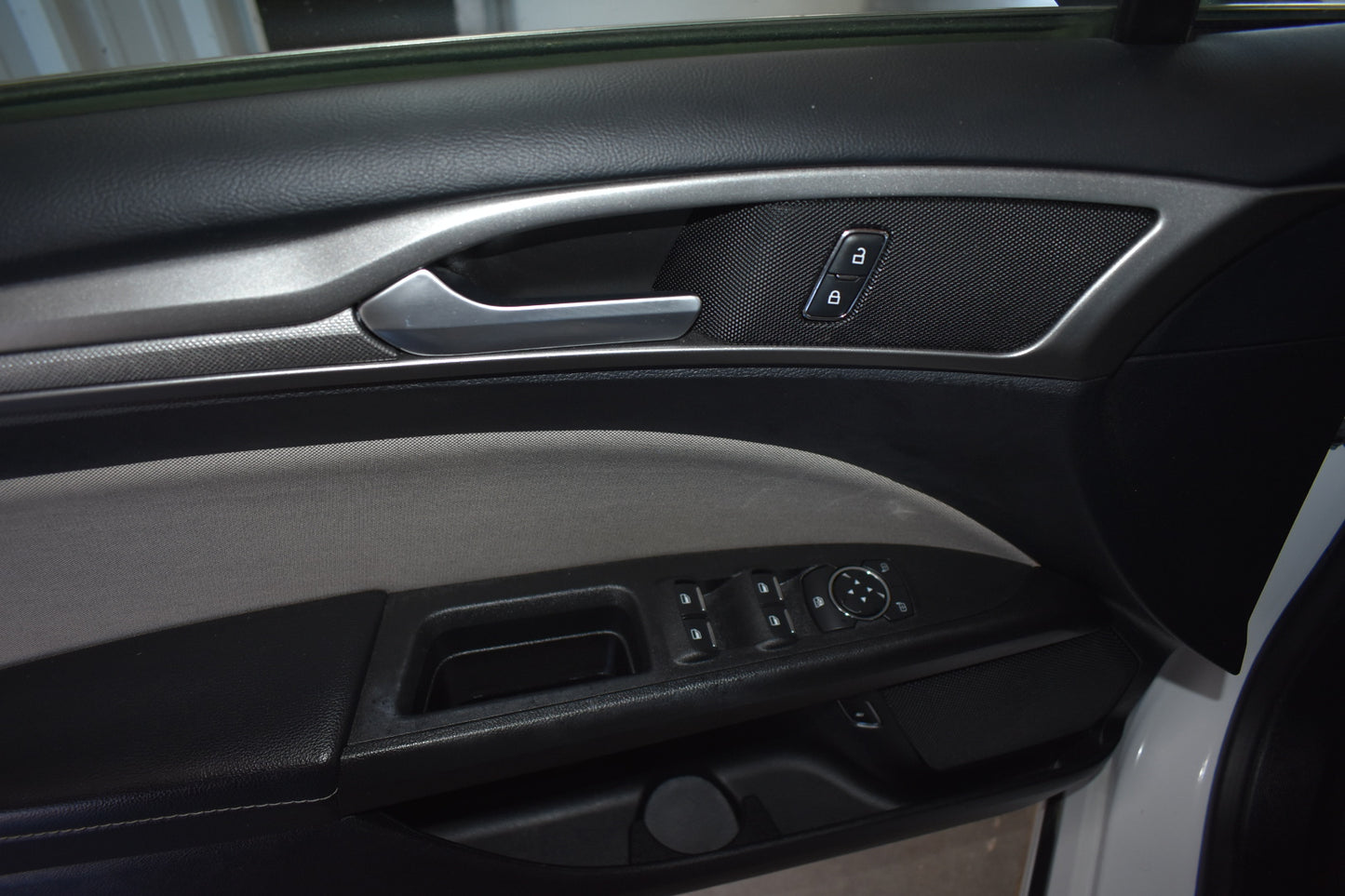 Close-up of a car's interior door panel with controls and handle.