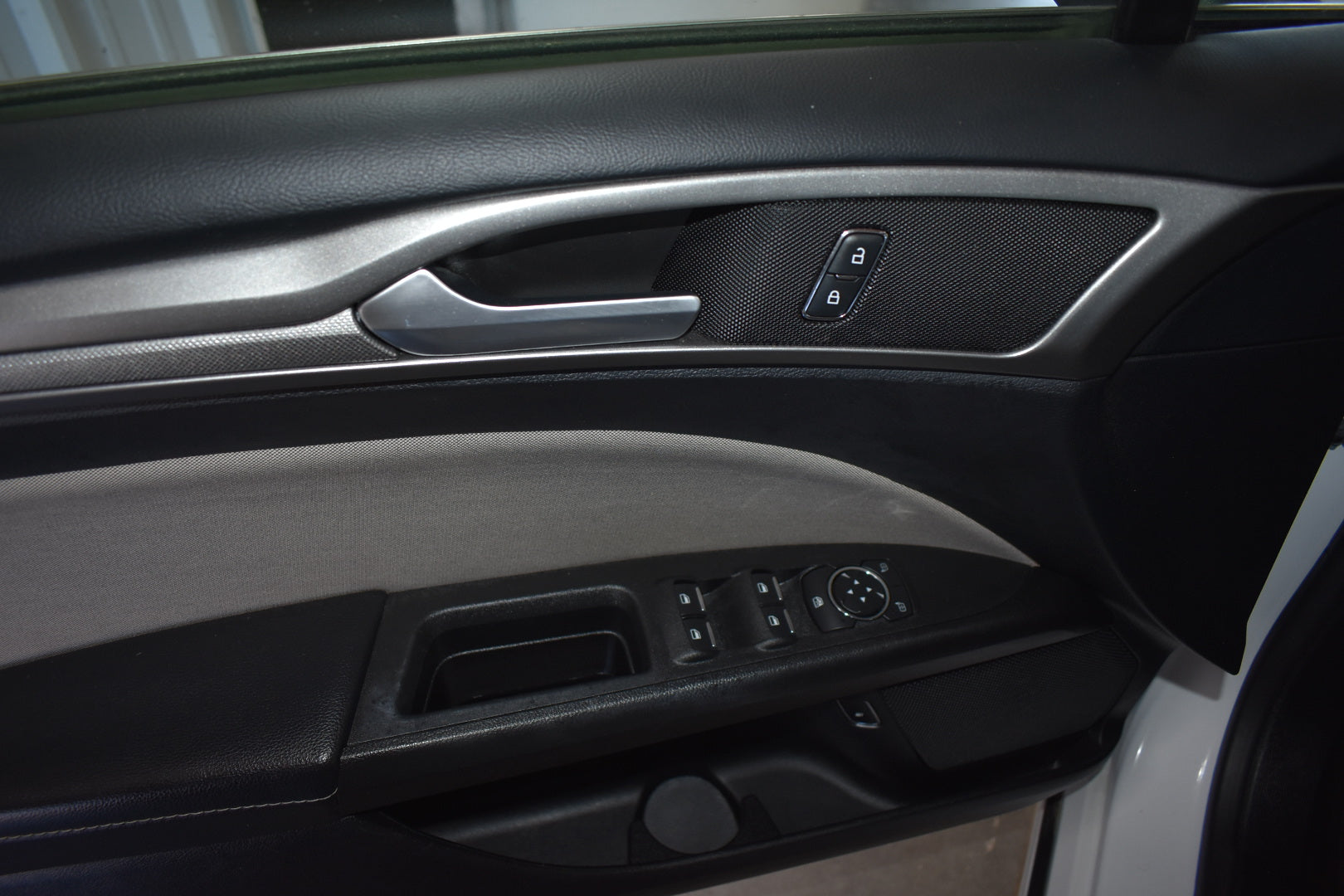 Close-up of a car's interior door panel with controls and handle.