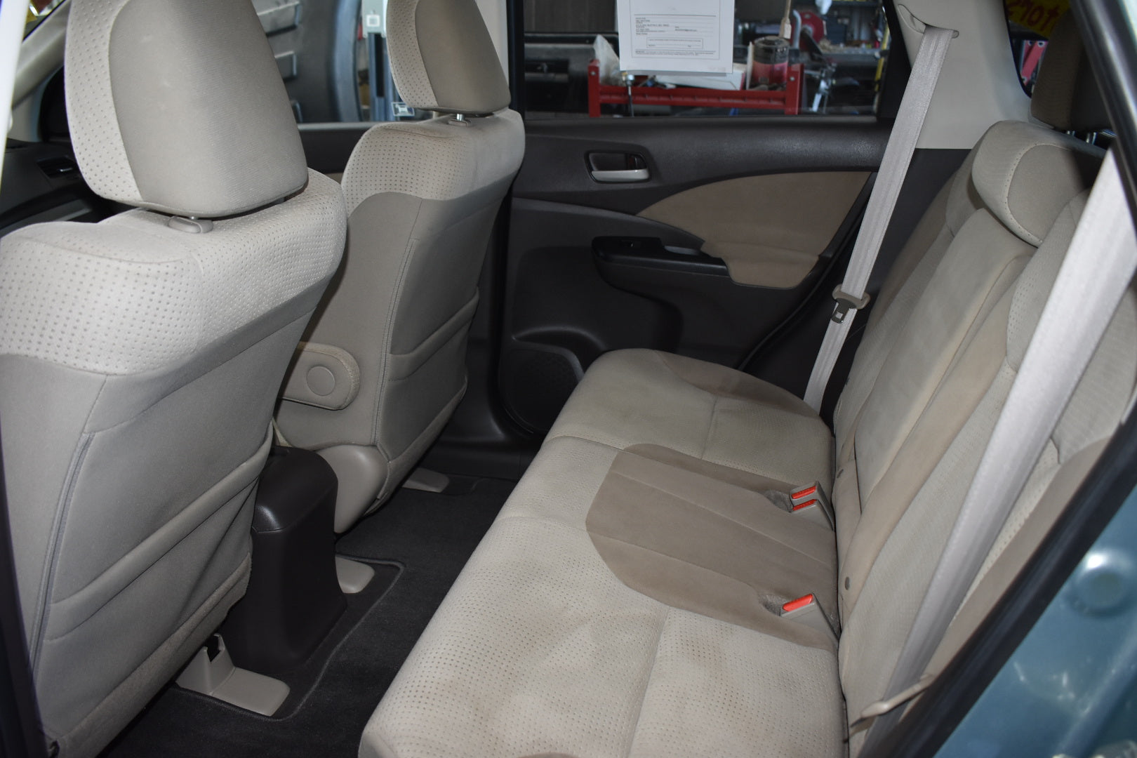 Back seat interior of a vehicle with beige seats and visible car parts.