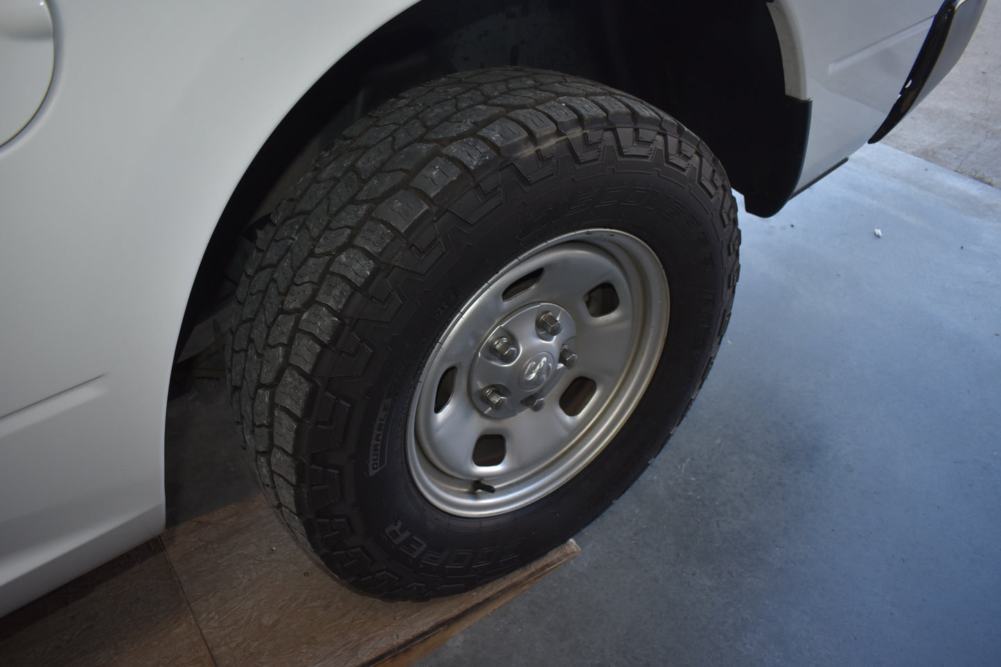 Close-up of a car tire on a white vehicle with a cardboard box underneath.
