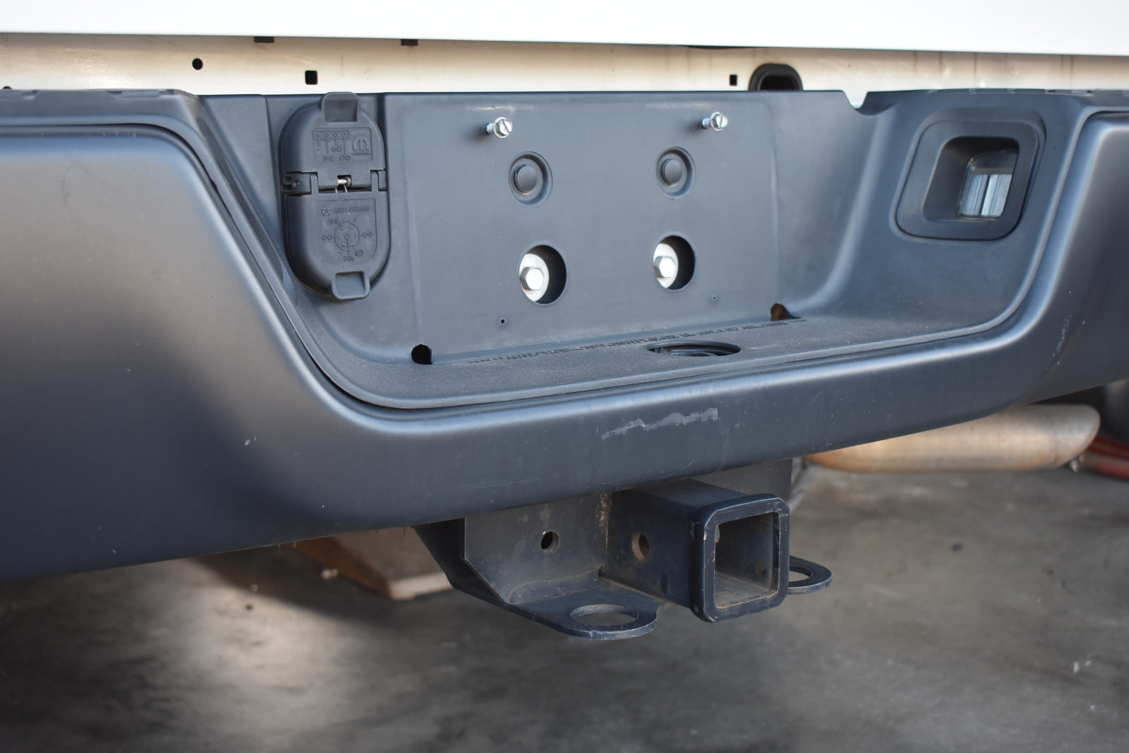 Close-up of a vehicle bumper with hitch receiver on a concrete floor.