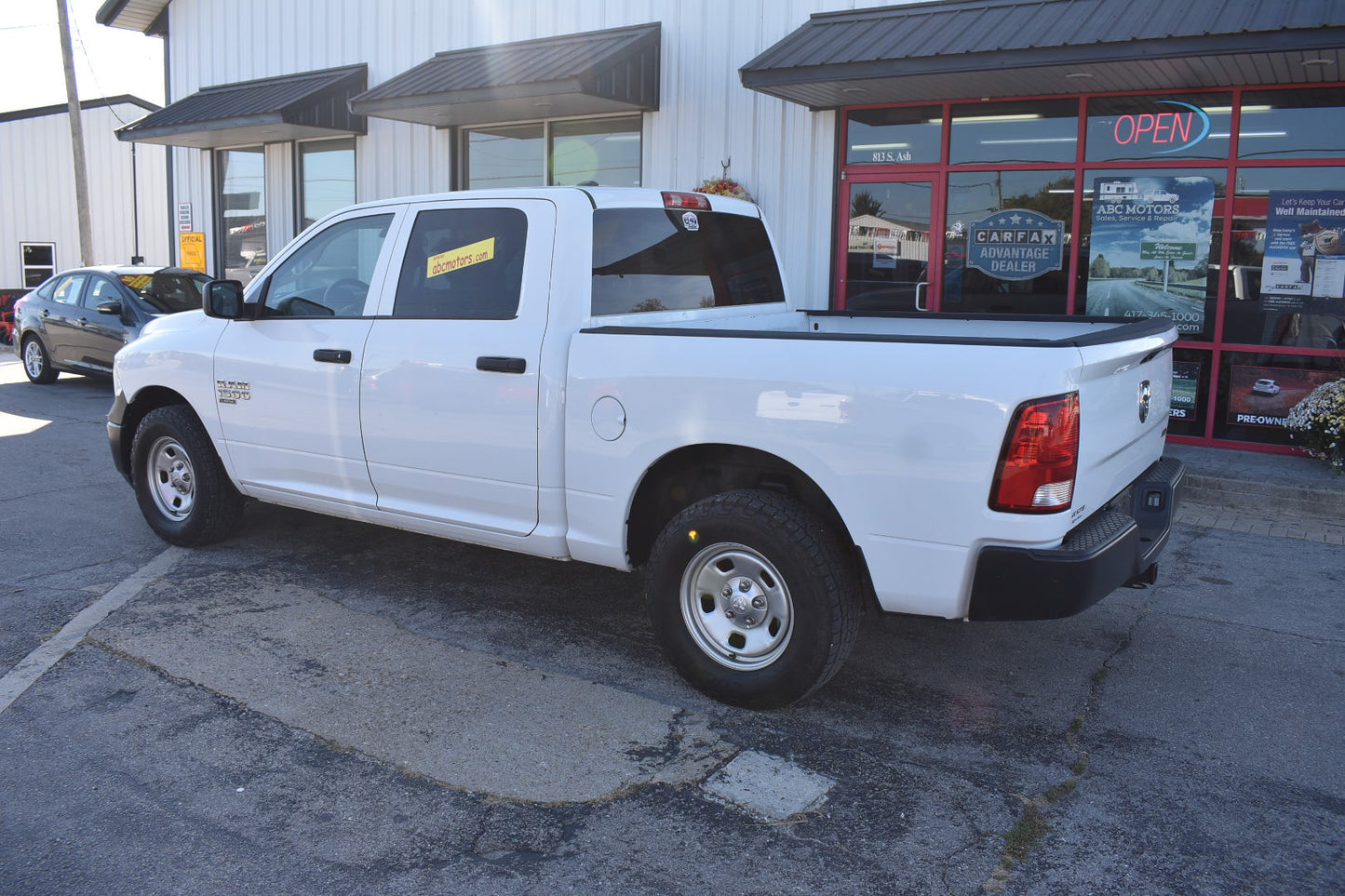 White pickup truck parked in front of a building with a 'Open' sign.