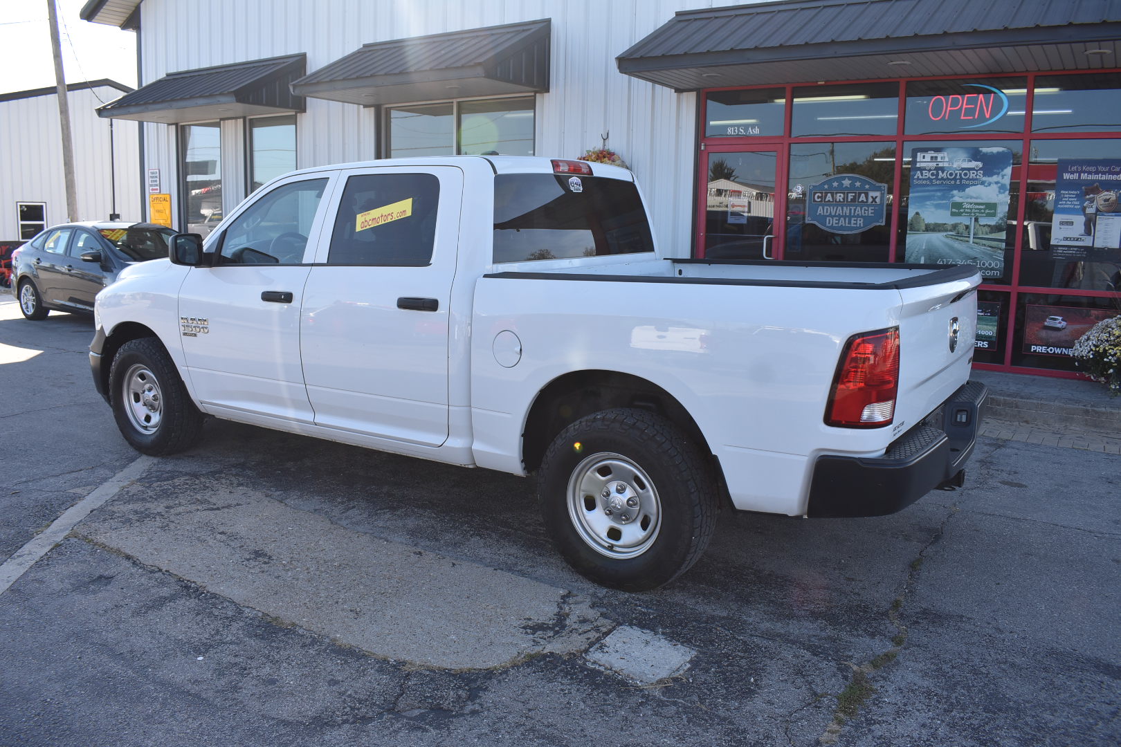 White pickup truck parked in front of a building with a 'Open' sign.