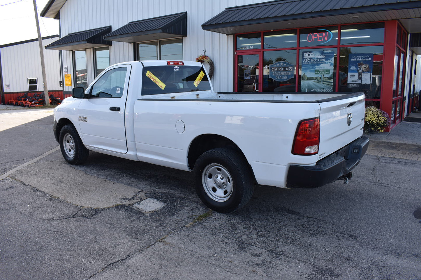 White pickup truck parked in front of a building with a 'Open' sign.