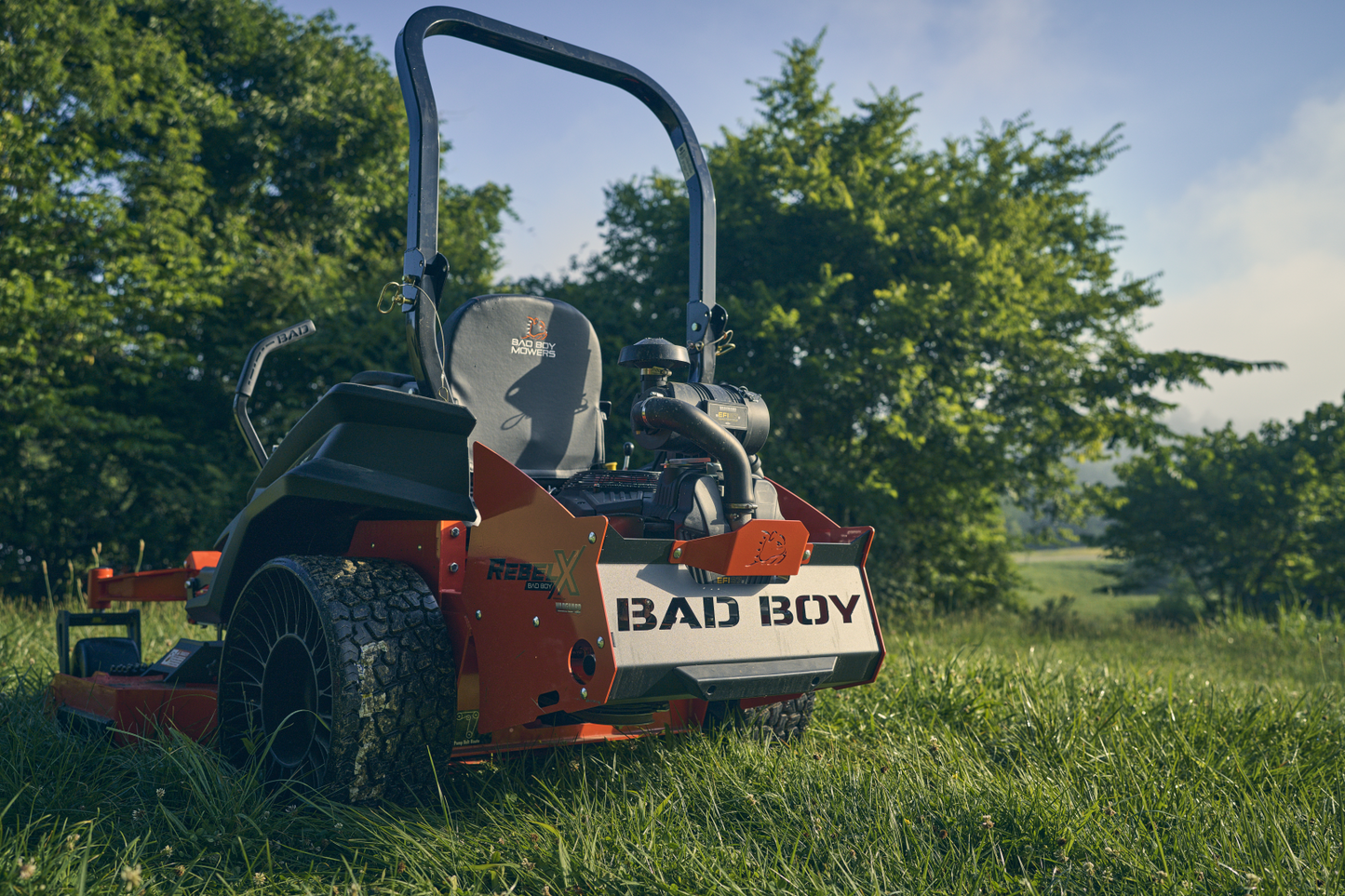 Orange Bad Boy mower in a grassy field with trees in the background