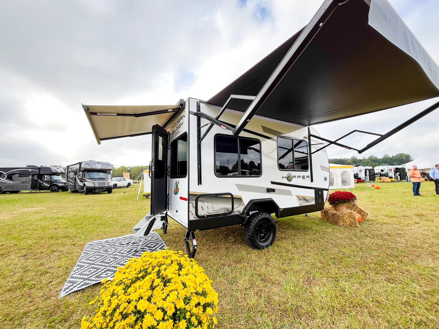Small travel trailer with an extended awning on a grassy field with other trailers in the background.