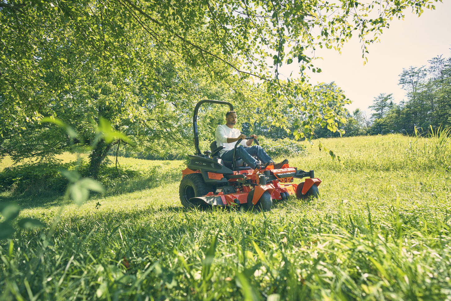 Person using a lawn mower in a grassy field with trees in the background