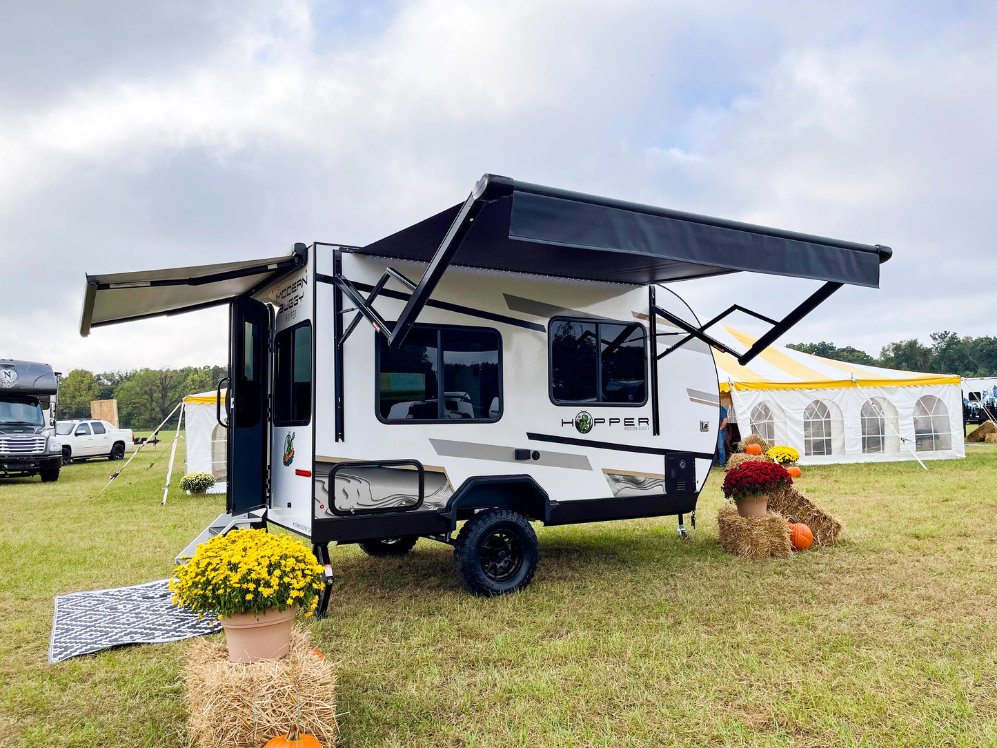 Small white travel trailer with an extended awning on a grassy field.