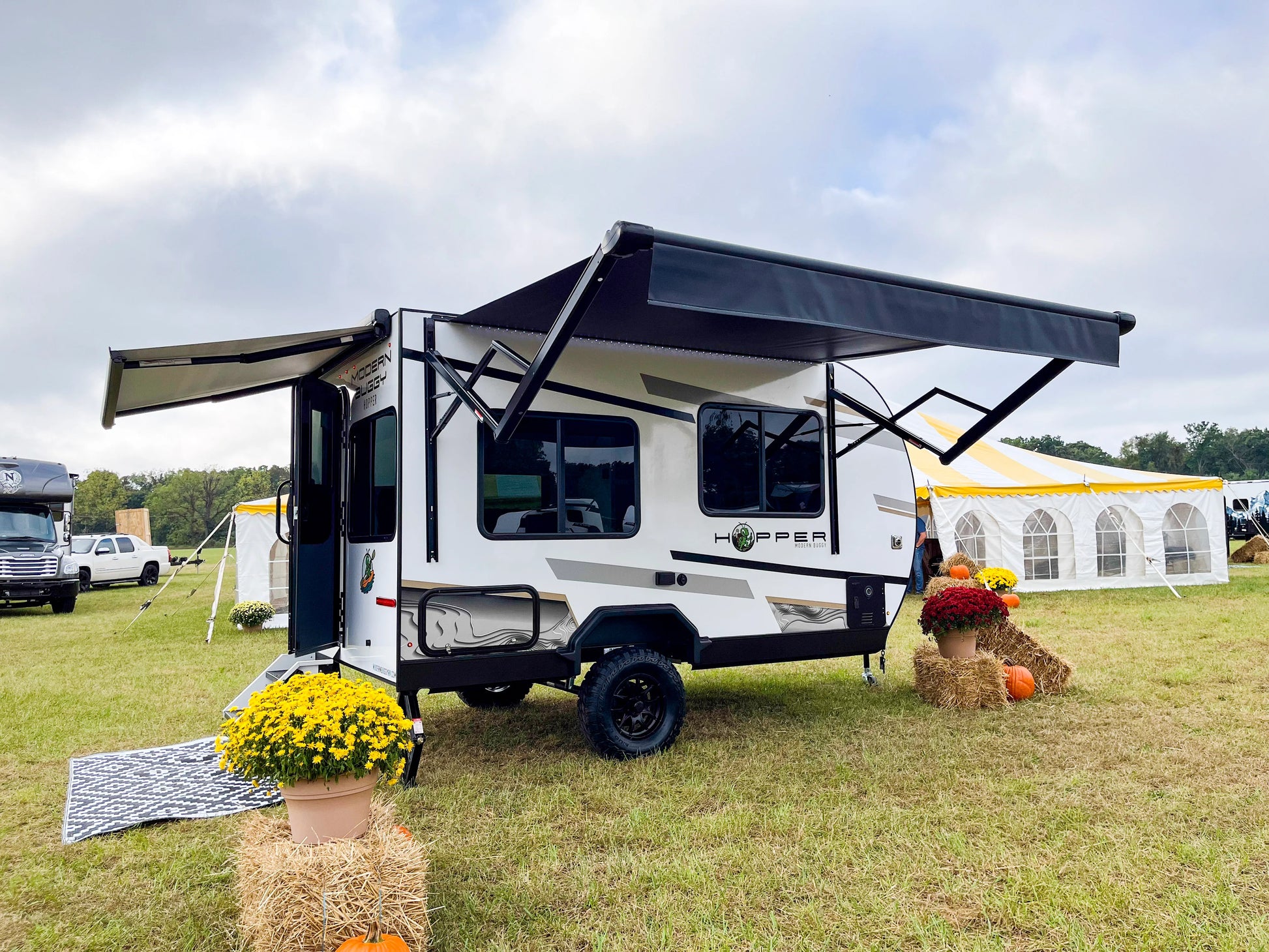 Small white travel trailer with an extended awning on a grassy field.