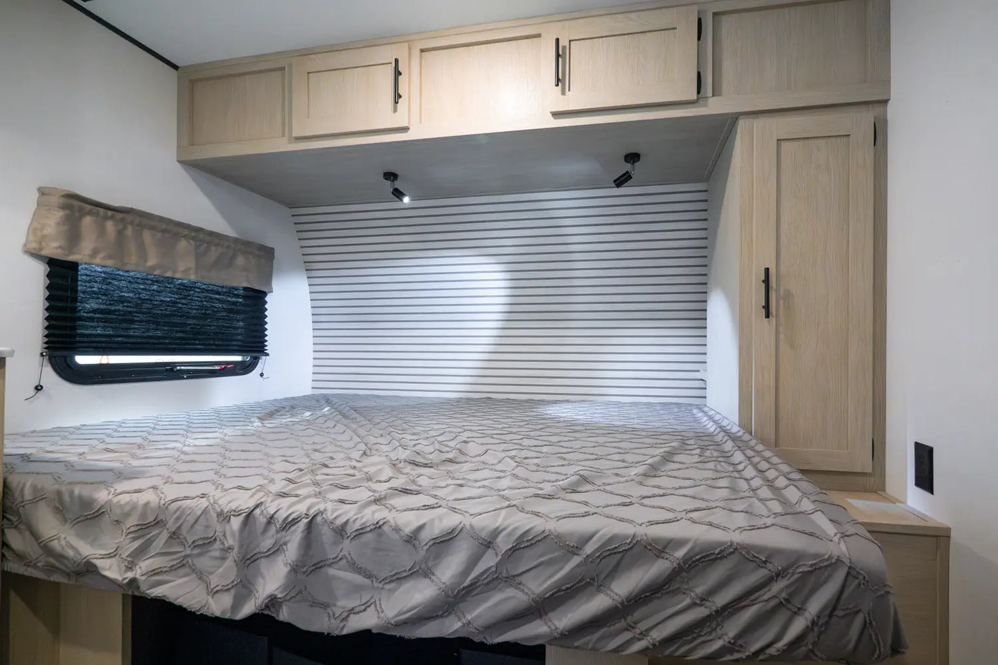 Compact bedroom setup inside a vehicle with a bed, cabinets, and window.