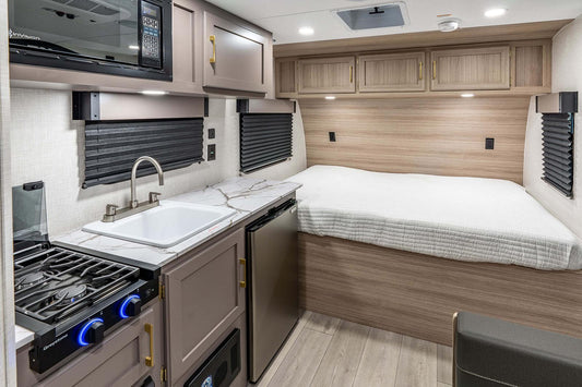 Compact living space inside a camper with kitchenette, bed, and storage cabinets.
