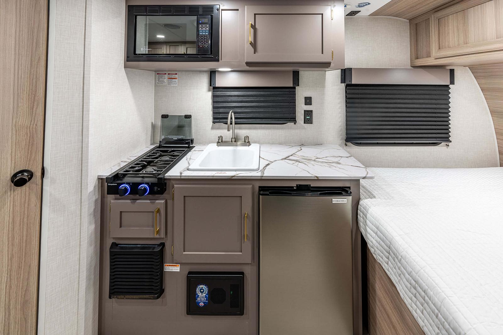 Compact kitchen area inside a recreational vehicle with stove, sink, and refrigerator.