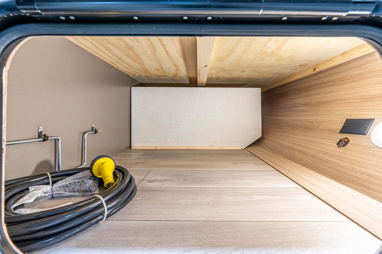 Underground room with wooden ceiling and floor, featuring plumbing and a hose.