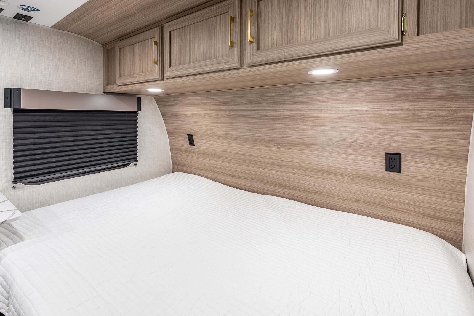 Bedroom interior of a vehicle with wooden cabinets and bed.
