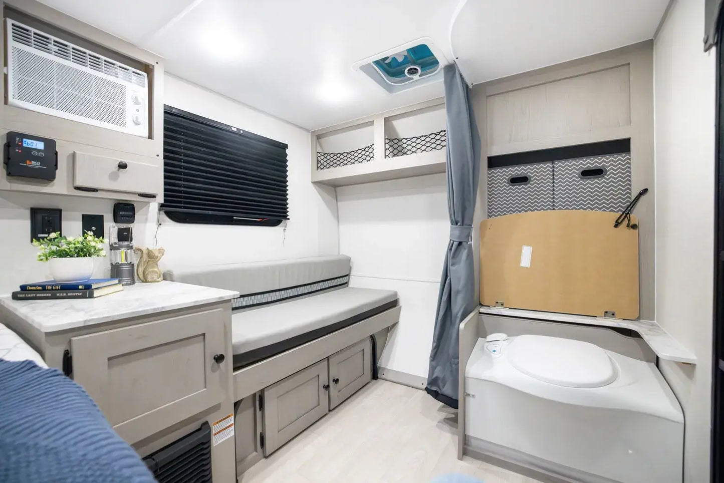 Compact interior of a camper with a bed, storage compartments, and a toilet.