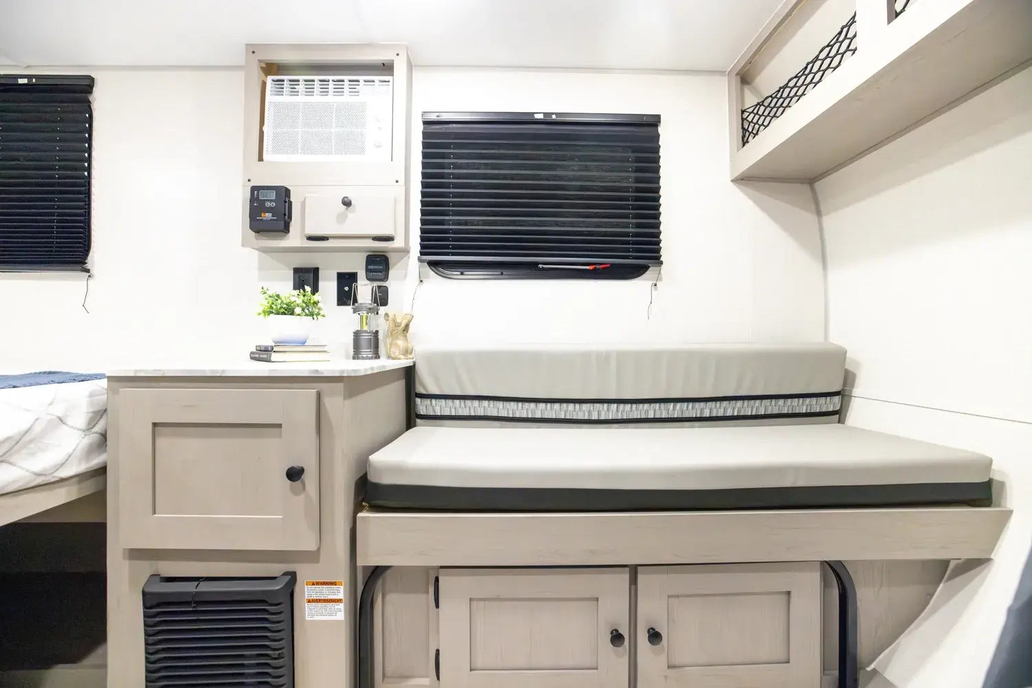 Compact living space with a bed, storage cabinets, and window blinds inside a vehicle.