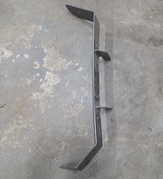 A dark gray metal bracket or support arm with multiple welded joints, photographed on a worn concrete floor.