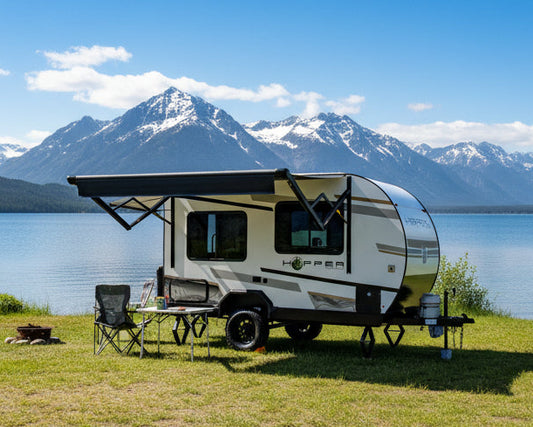 Small travel trailer with an extended awning on a grassy area with RVs in the background.