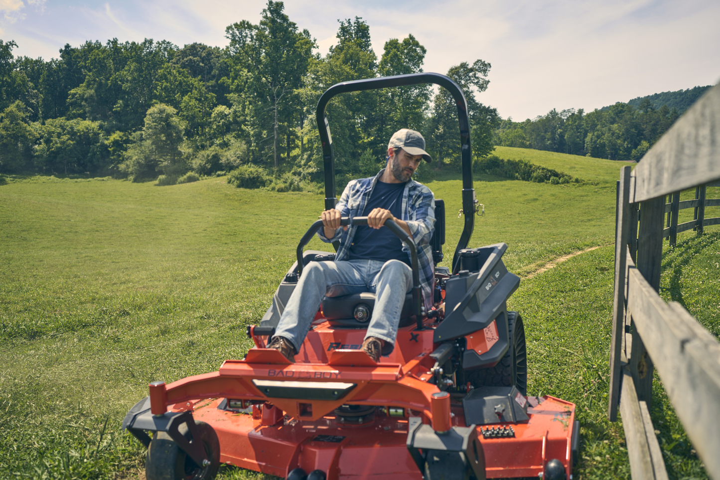 Man operating a red lawn mower in a grassy field with trees in the background