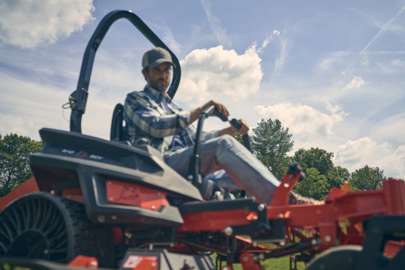 Man operating a red tractor in an open field with a blue sky.