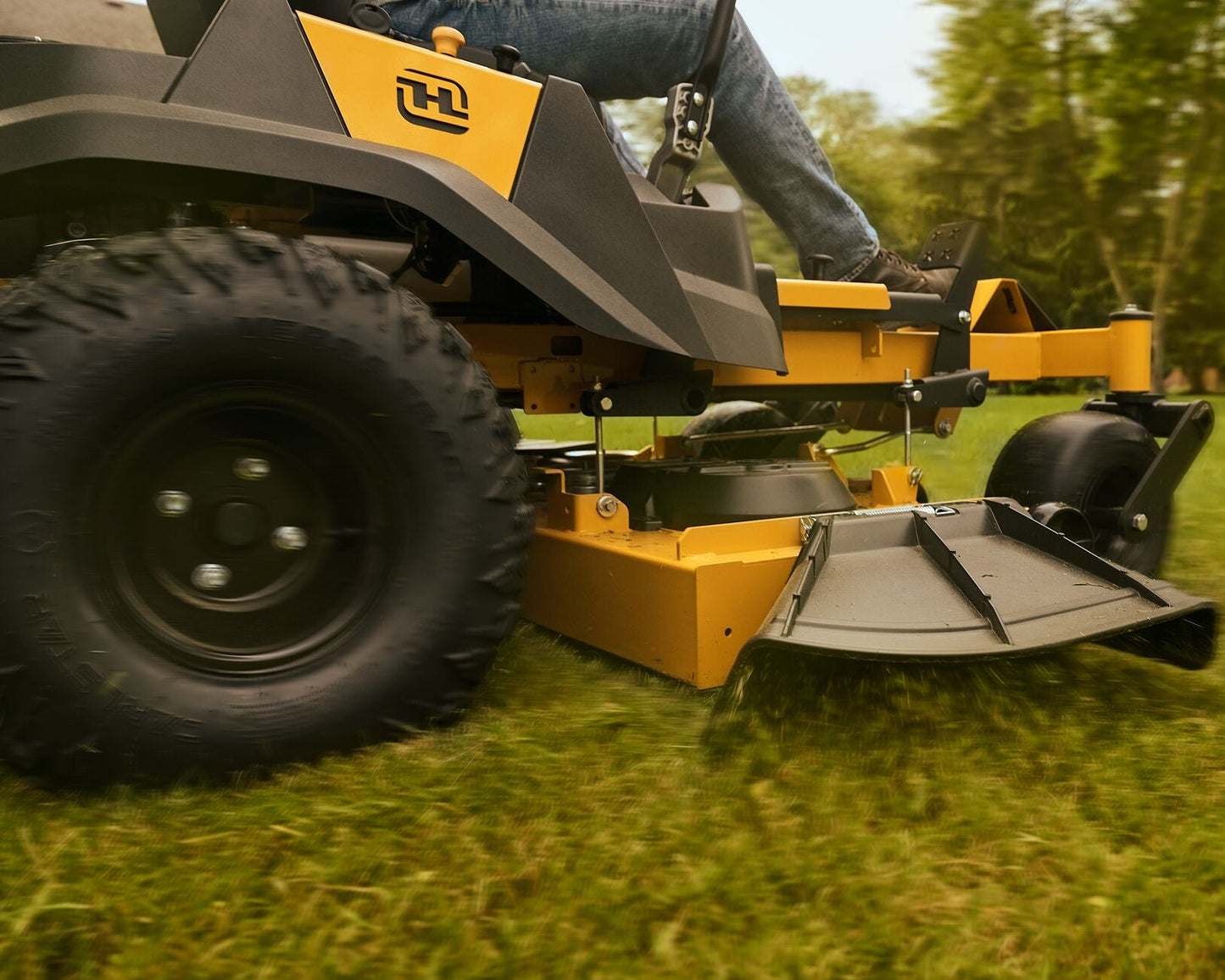 Person operating a yellow and black lawn mower on grass with trees in the background