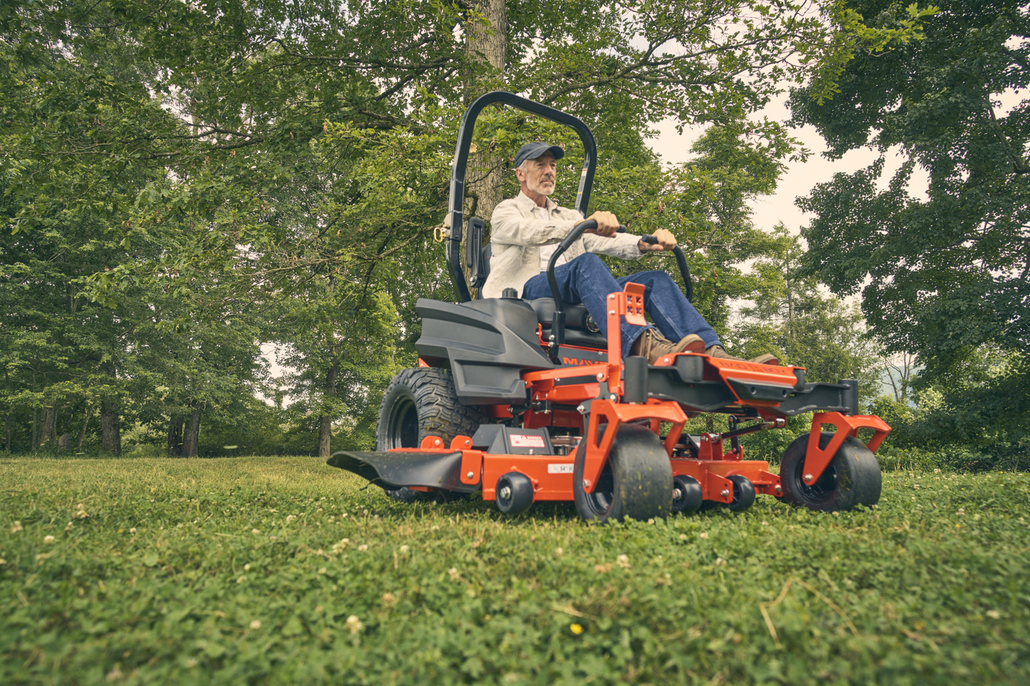 Man operating a red riding lawn mower in a grassy area with trees in the background