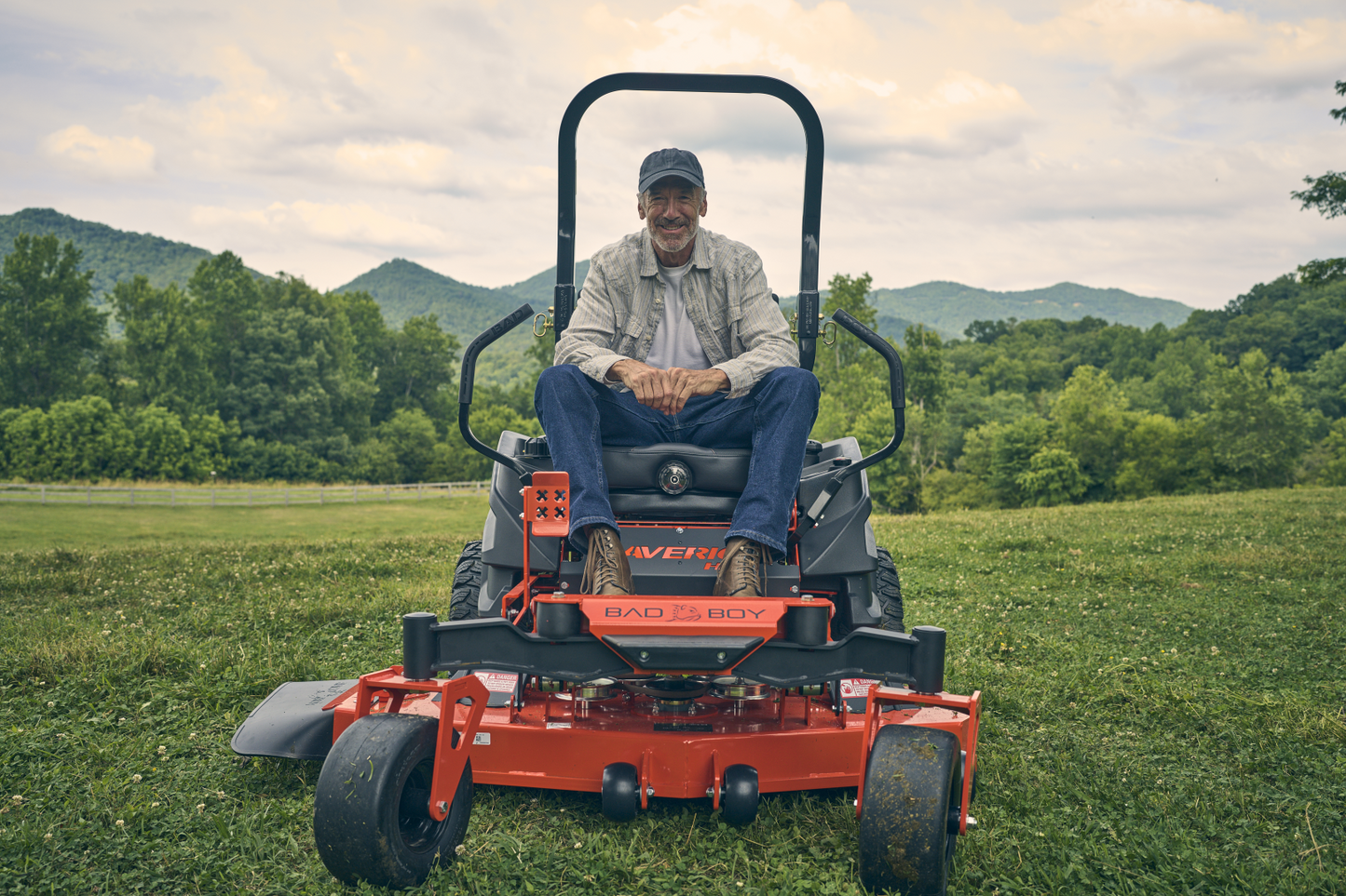Man sitting on a riding lawn mower in a grassy field with mountains in the background