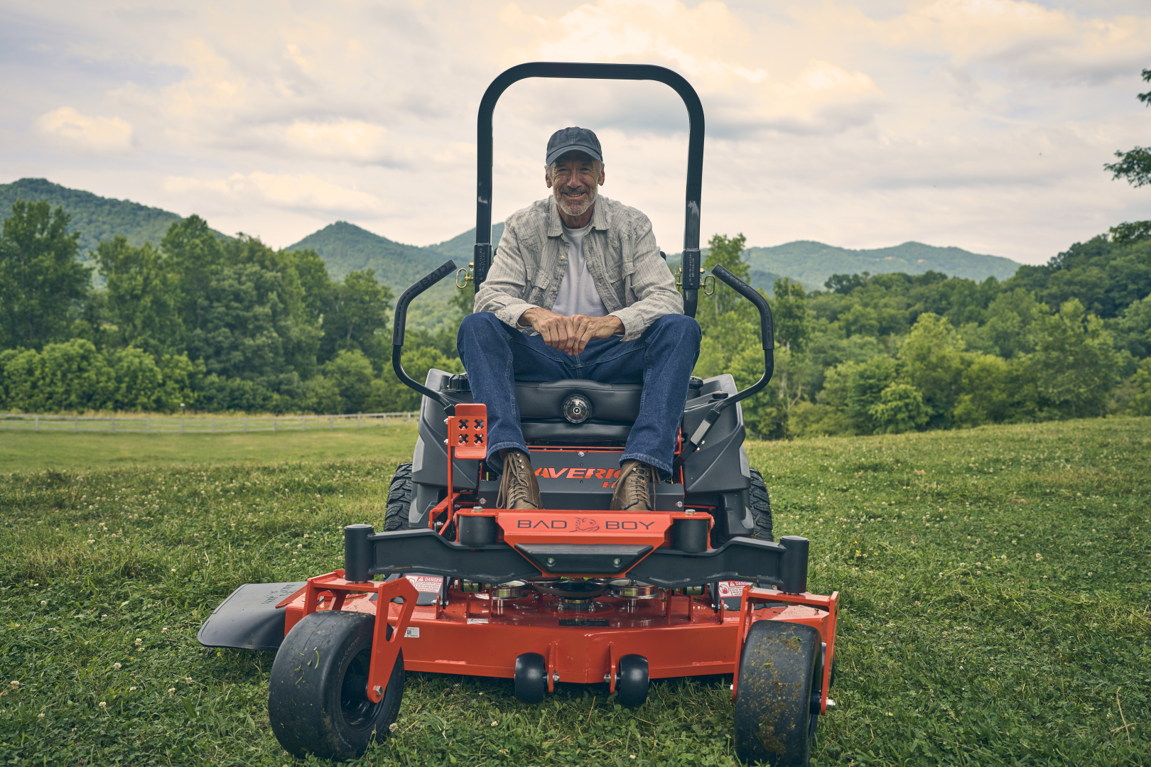 Man sitting on a riding lawn mower in a grassy field with mountains in the background