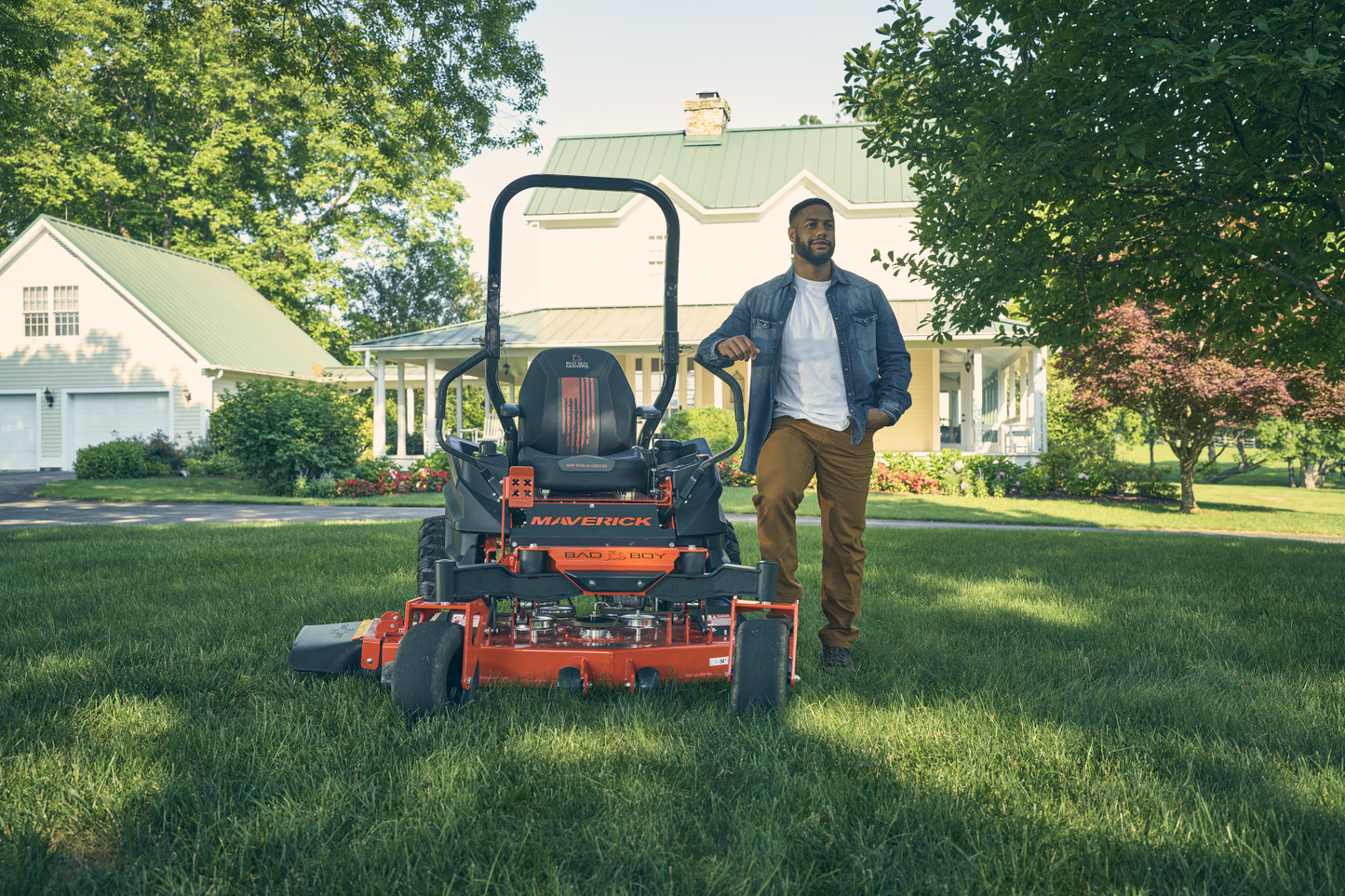 Man standing next to a lawn mower on a grassy lawn with a house in the background