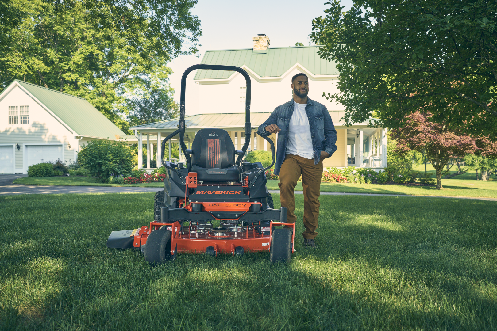 Man standing next to a lawn mower on a grassy lawn with a house in the background