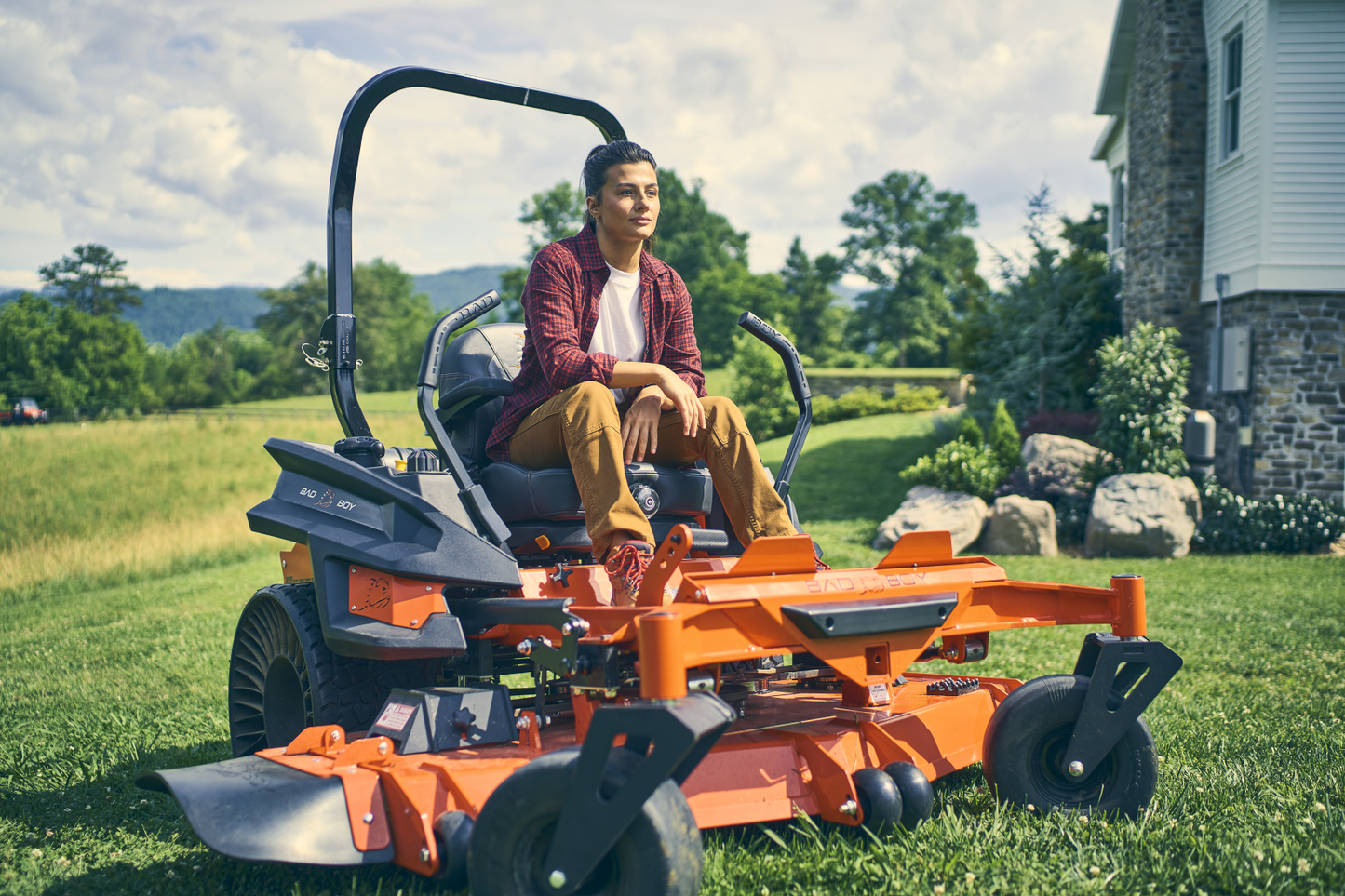 Person operating a large orange lawn mower in a grassy area with a house in the background