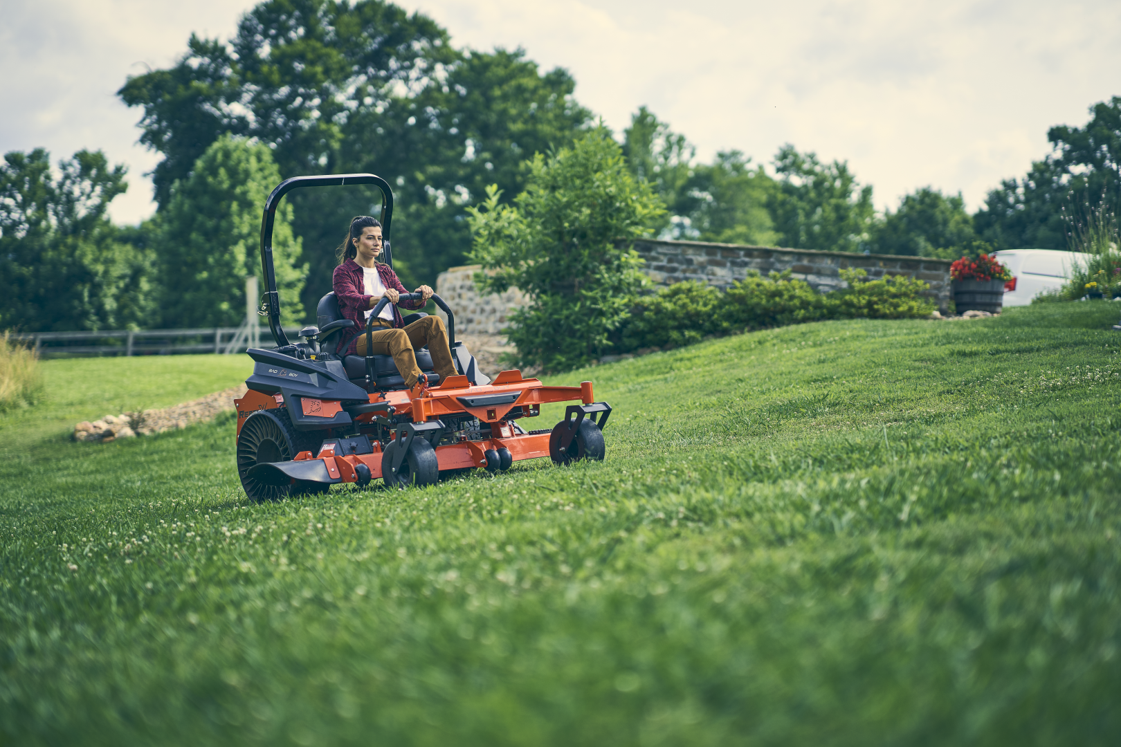 Person operating a lawn mower on a grassy field with trees in the background