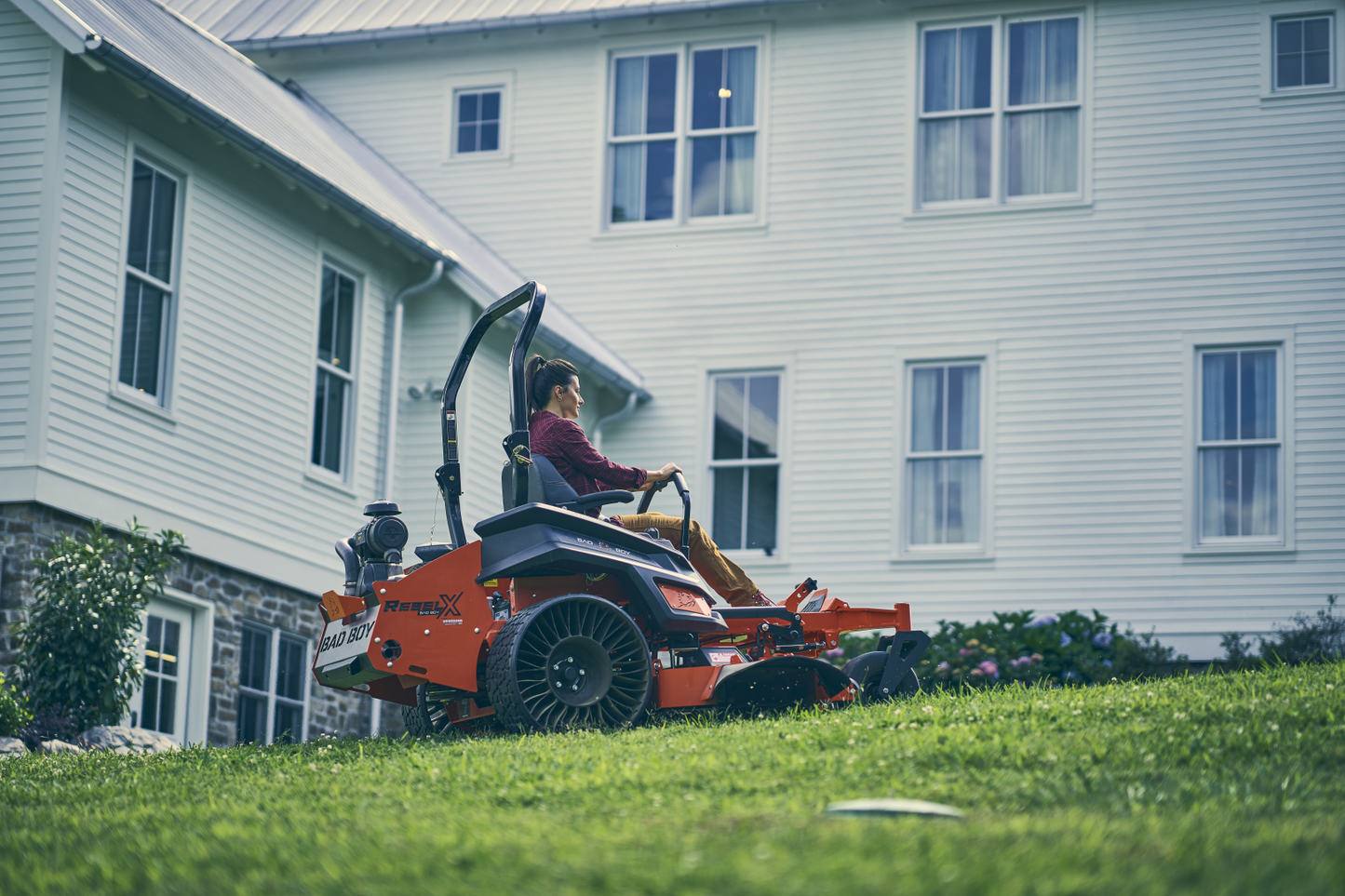 Person using a riding lawn mower in front of a house