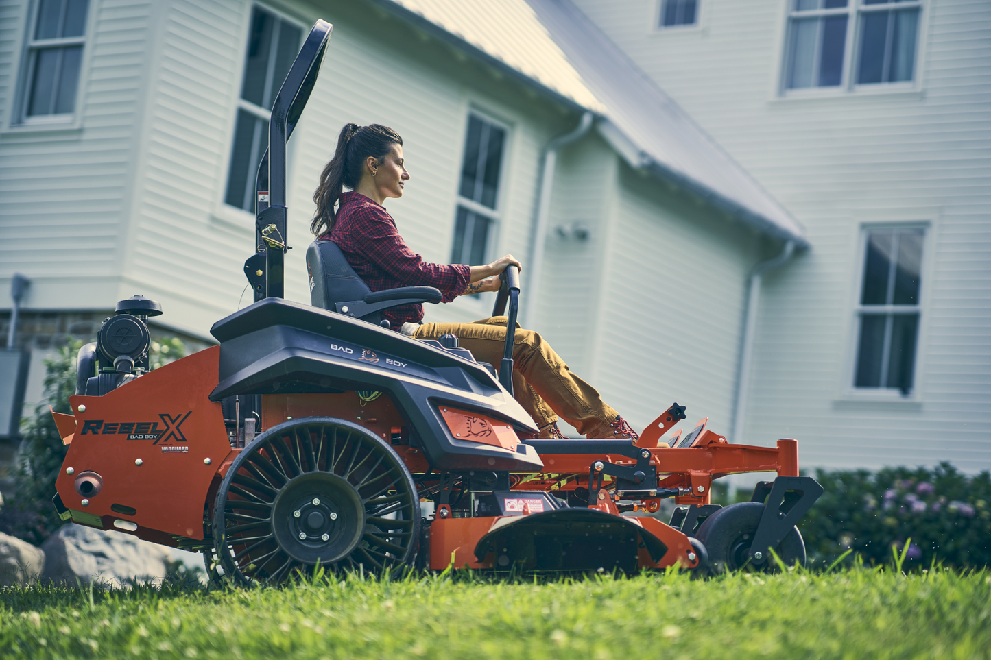 Person operating a large orange lawn mower in front of a house