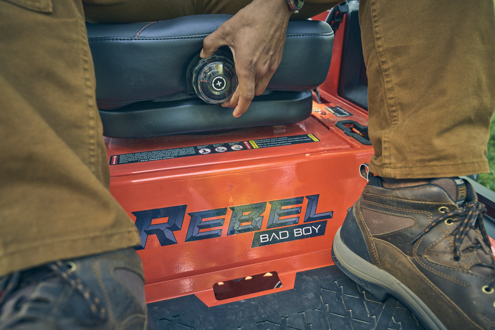 Person using a tool on a red 'Rebel Bad Boy' machine, wearing brown pants and boots.