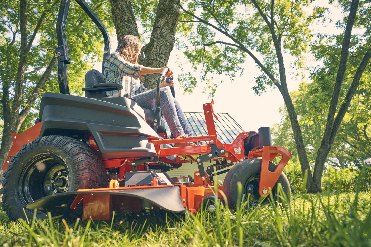 Person operating a red riding lawn mower in a park-like setting with trees and grass.