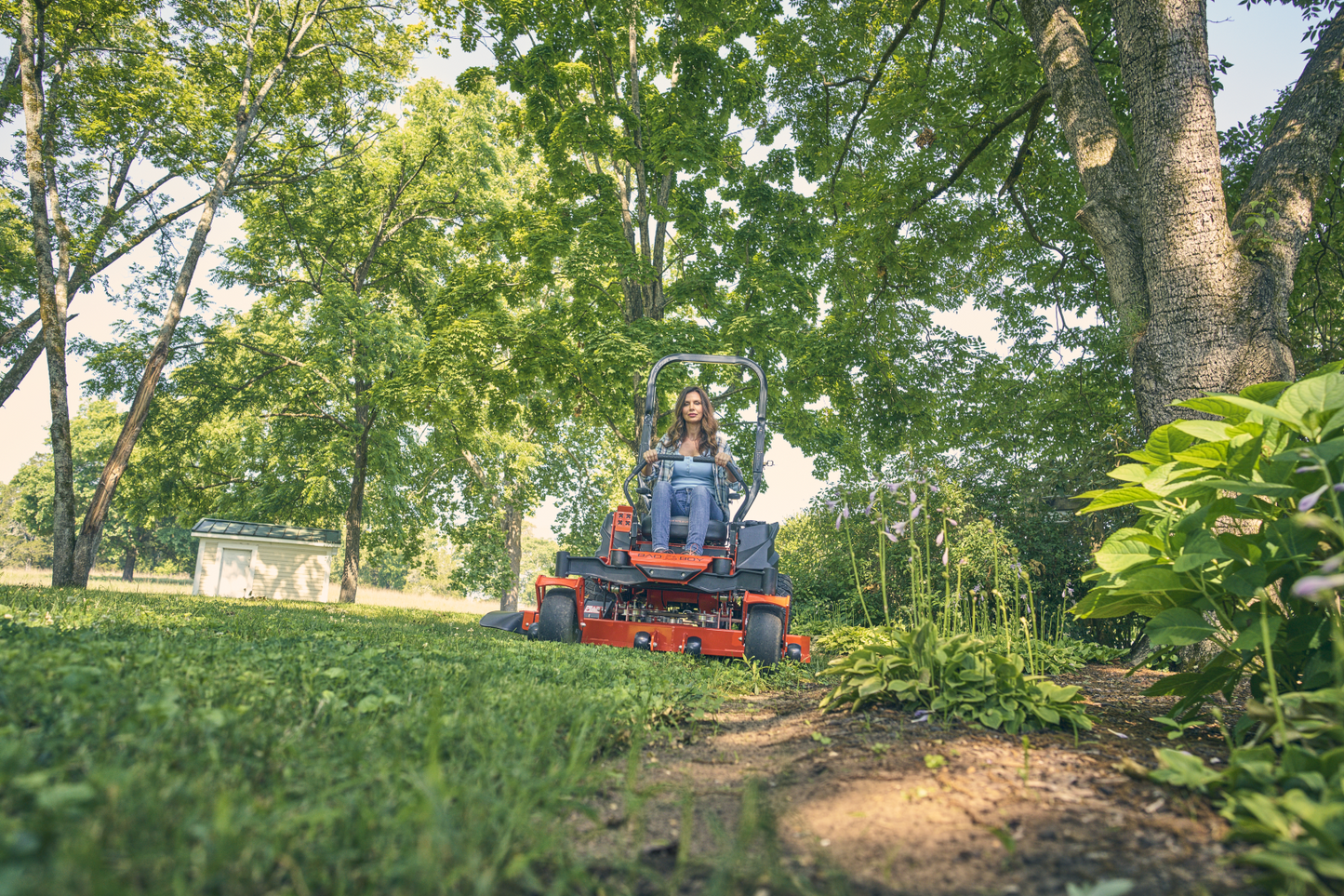 Person operating a small tractor in a lush green garden with trees in the background